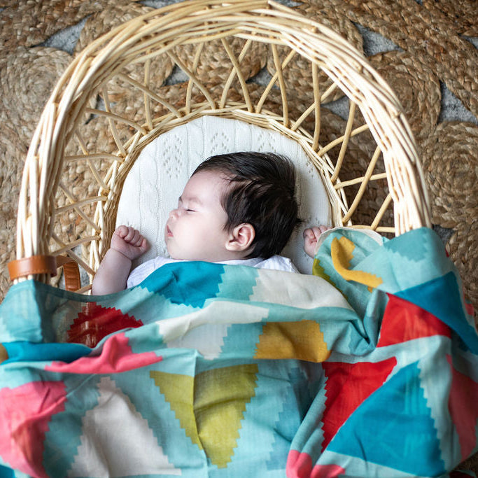 Baby sleeping in a moses basket with a Green Aztec Muslin