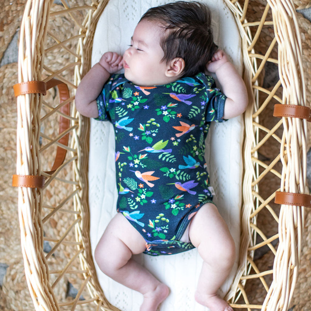 Baby in a wicker crib with a colorful onesie
