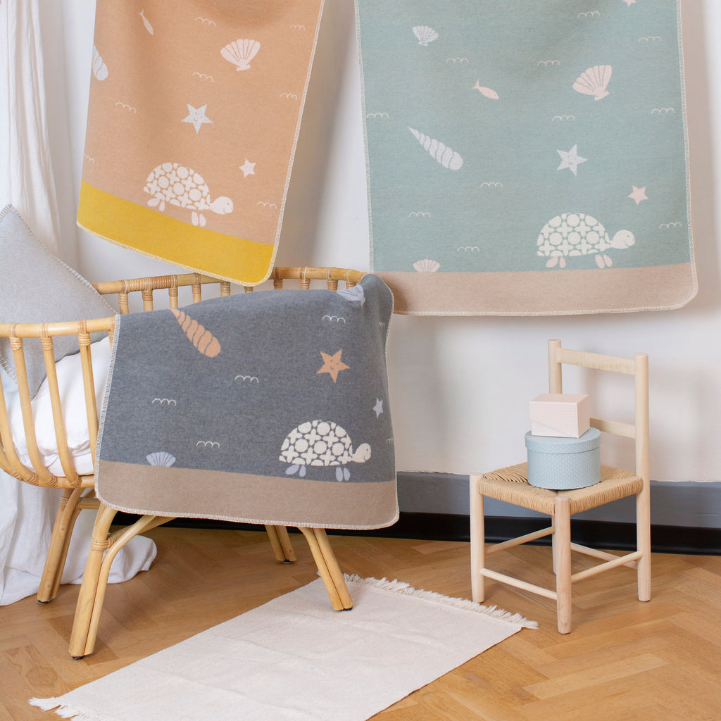 Three baby blankets with turtle patterns hanging on a rack in a nursery.