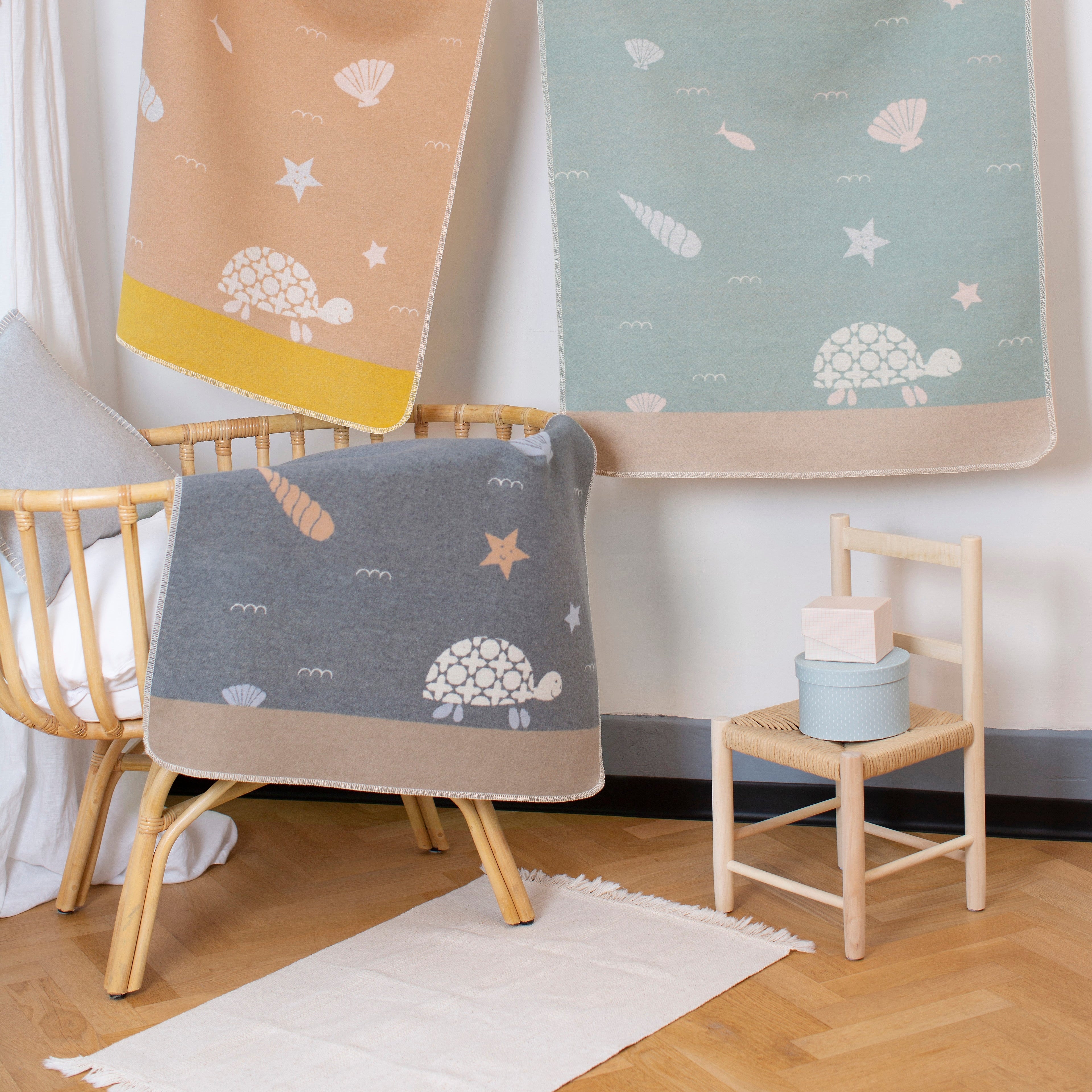 Three baby blankets with turtle patterns hanging on a rack in a nursery.