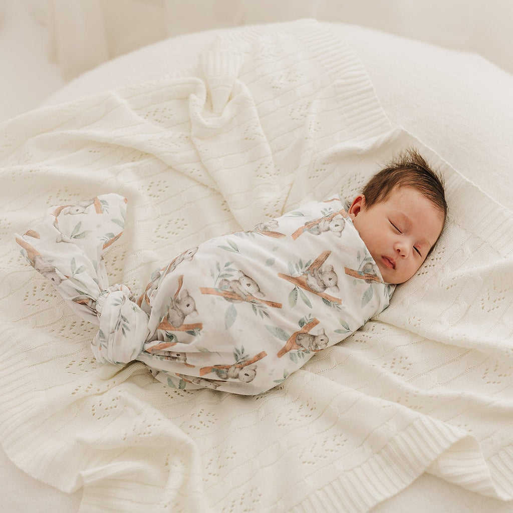 Newborn baby swaddled in a koala muslin on the cream fern blanket.