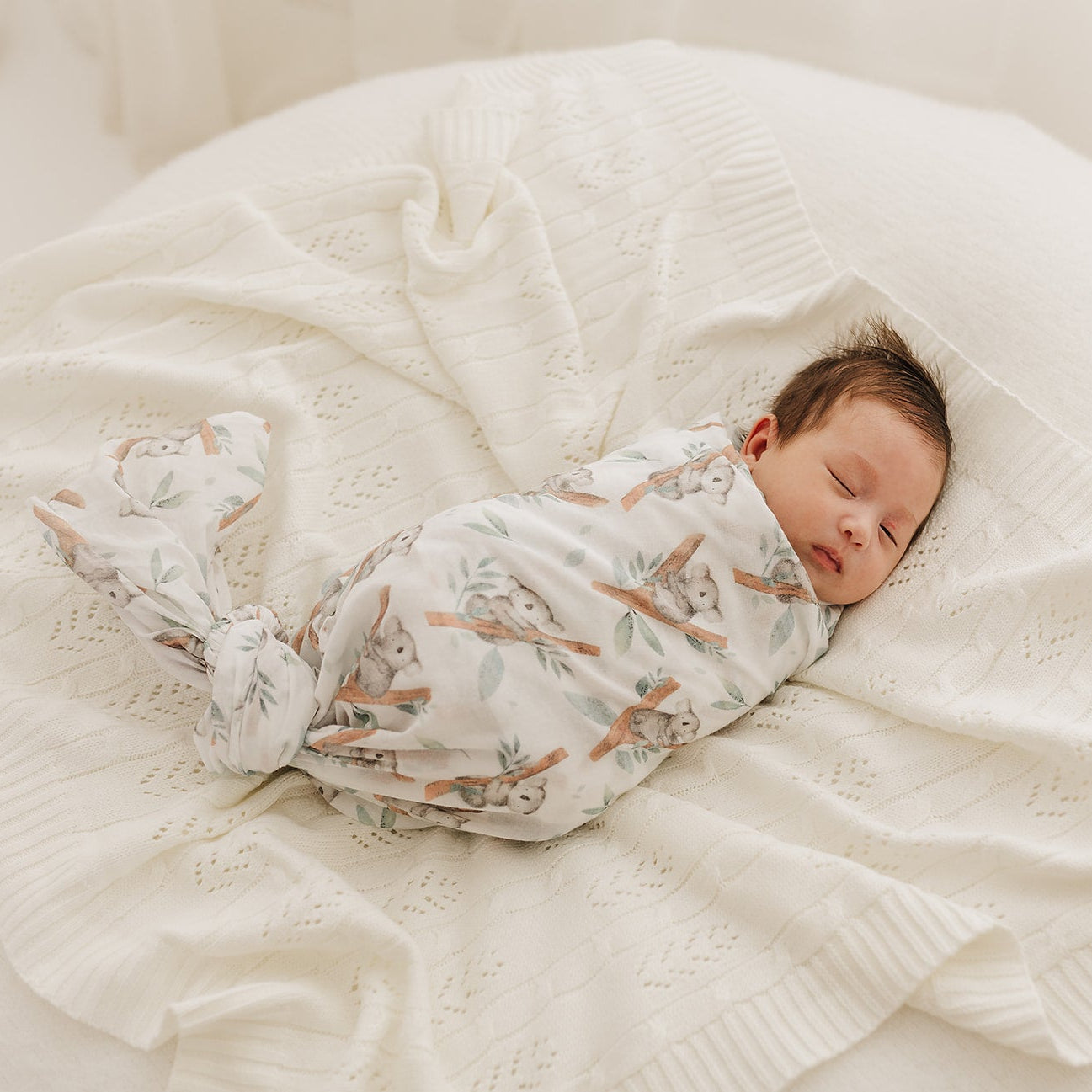 Newborn baby swaddled in a koala muslin on the cream fern blanket.