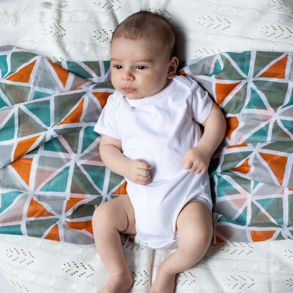 Baby in a white bodysuit lying on a  geometric muslin.
