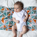 Baby in a white bodysuit lying on a  geometric muslin.